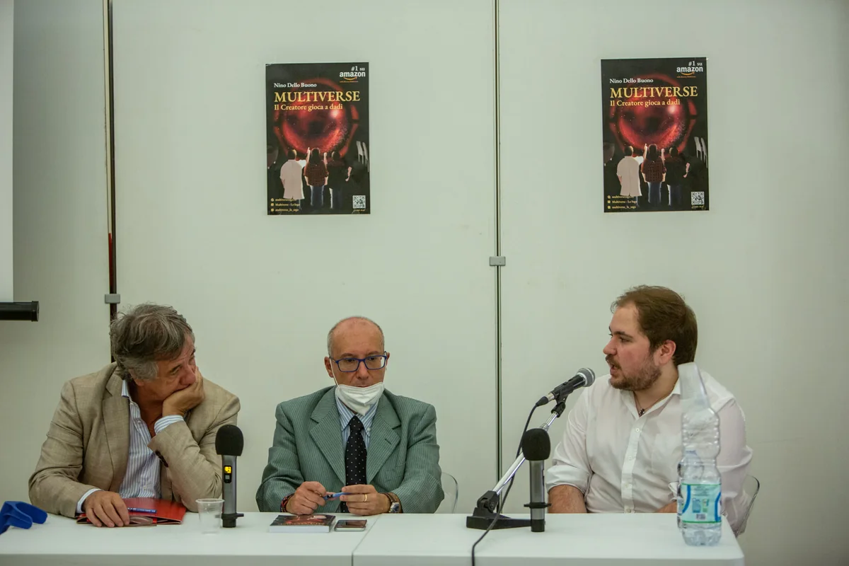 Da sinistra a destra, Giuseppe
          Merlino, Lorenzo Calò e Nino Dello Buono seduti al tavolo con i microfoni, due manifesti di
          MULTIVERSE appesi alla parete alle loro spalle.