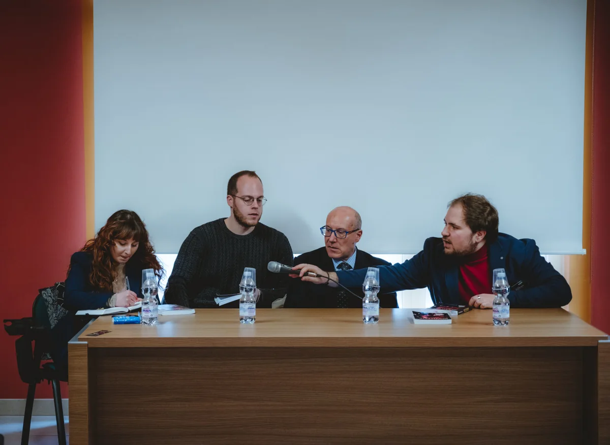 Da sinistra a destra, Maria
          Barbone, Gerardo Varallo, Lorenzo Calò e Nino Dello Buono tra il telo di un proiettore e un
          tavolo. Dello Buono sta passando il microfono a Barbone.